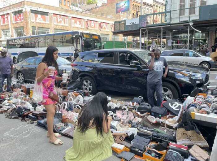 A group of people standing on the sidewalk near a pile of shoes

Description automatically generated